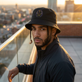 Man wearing a black bucket hat with a logo on a rooftop with cityscape background