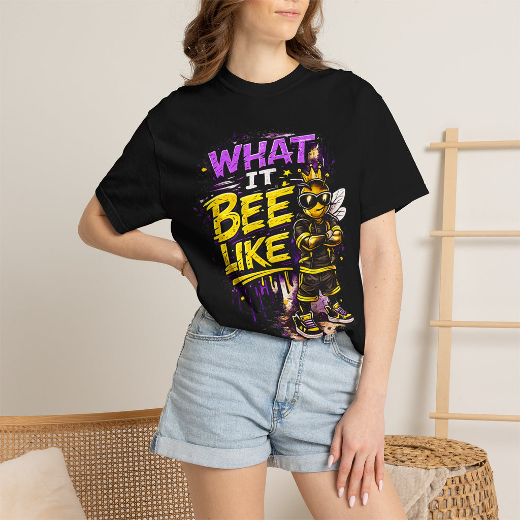 A woman wearing a black graphic t-shirt with a colorful bee design and the text 'WHAT IT BEE LIKE' in purple and yellow, paired with light blue denim shorts.